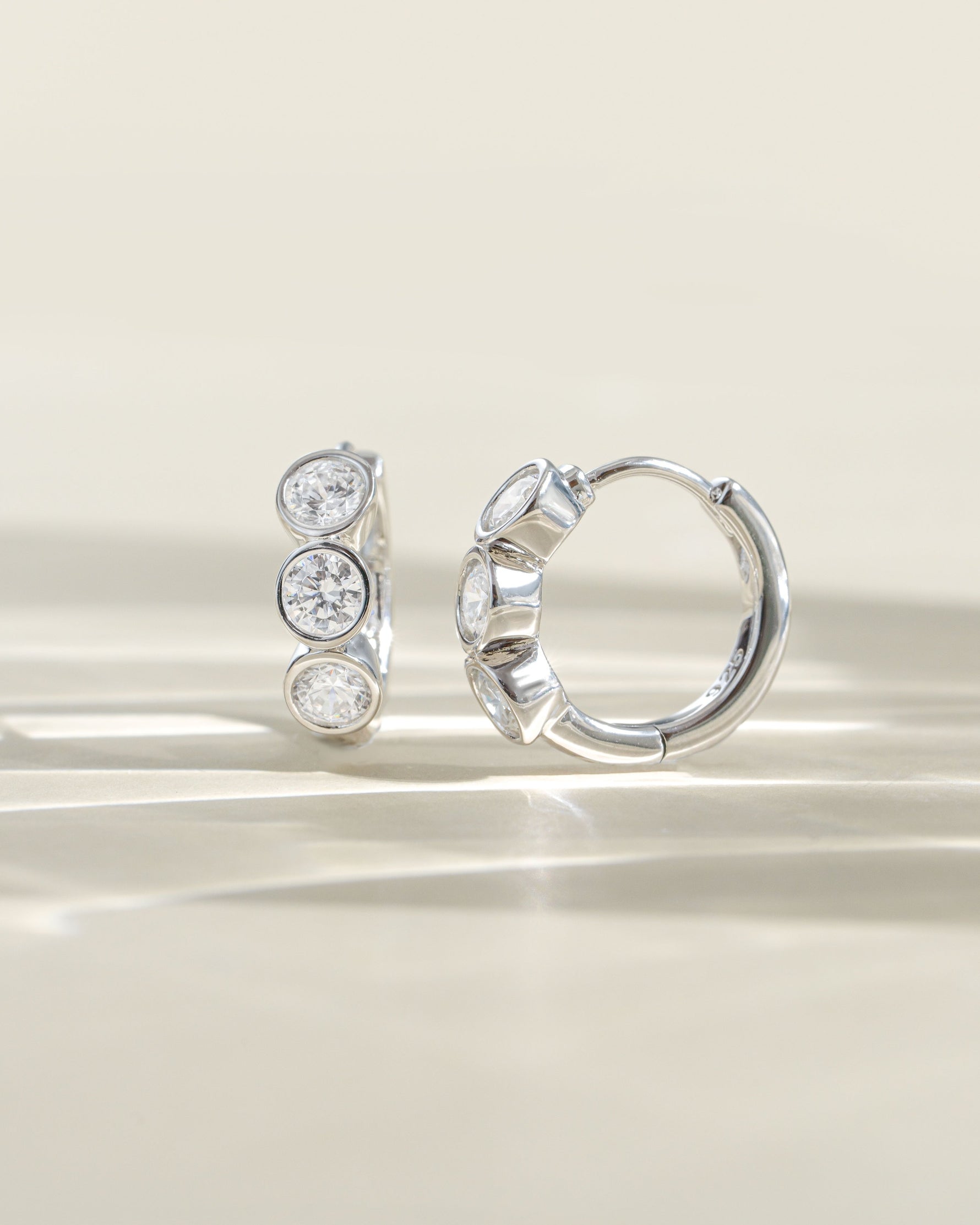 Side view of Sami Jewels Bezel 3 Stone Huggie Hoop Earrings featuring three sparkling stones on small gold hoops.