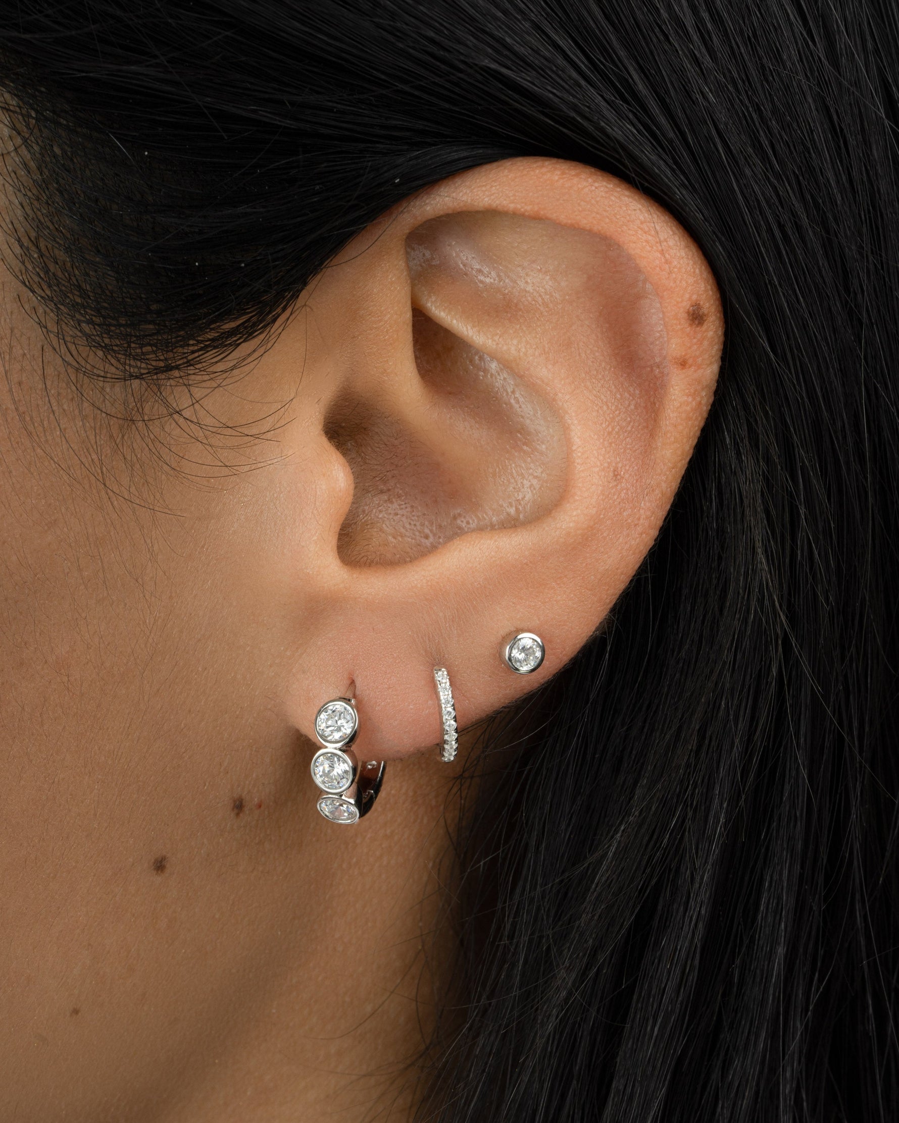 Sterling silver Bezel 3 Stone Huggie Hoop Earrings by Sami Jewels, shown on a model with small, stylish hoop earrings.