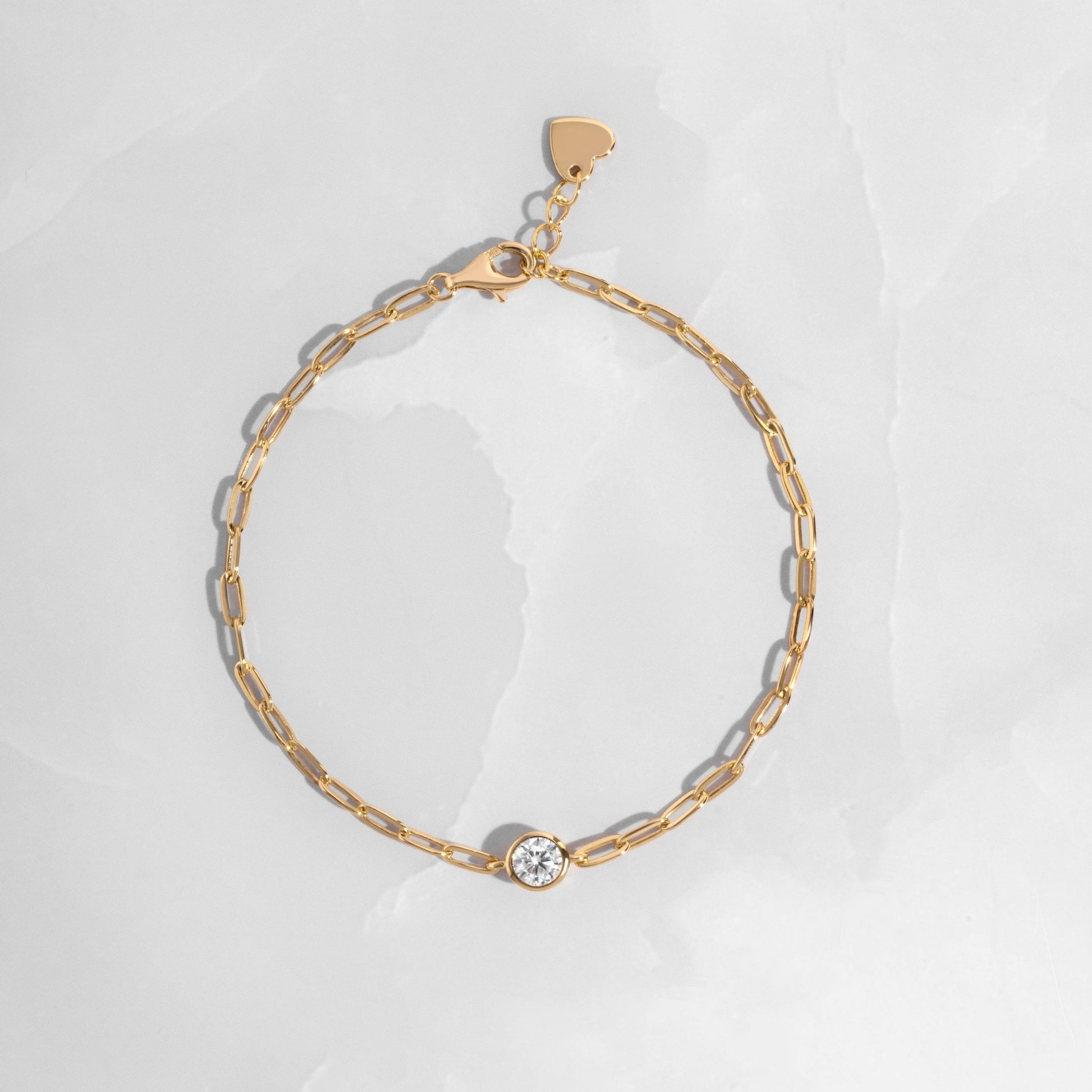 Gold chain bracelet with a bezel charm on white marble background