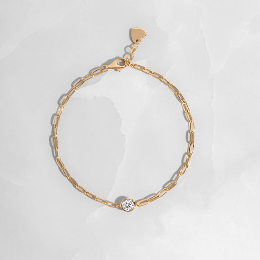 Gold chain bracelet with a bezel charm on white marble background