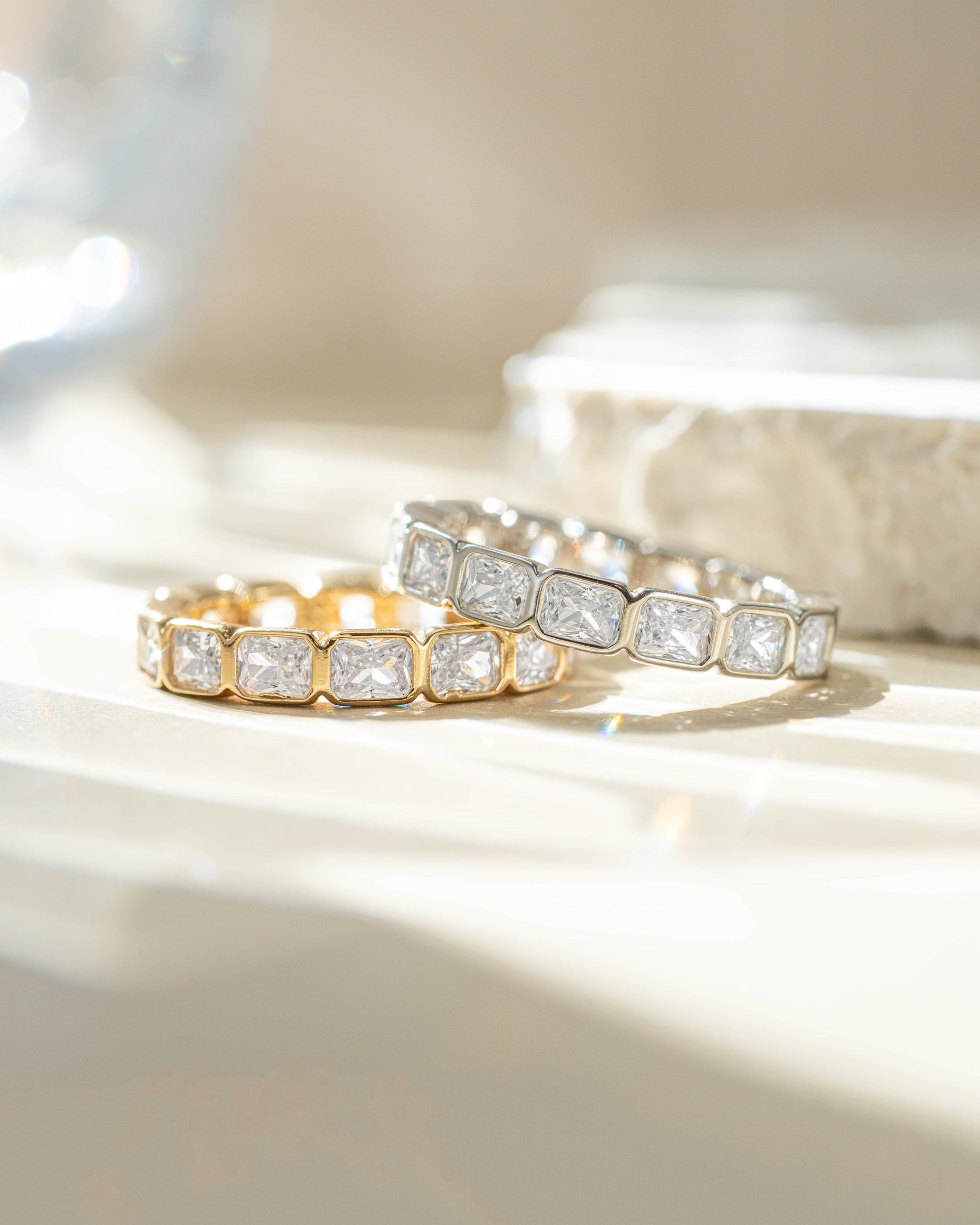 Close-up of Sami Jewels bezel emerald cut eternity band ring featuring gold and sterling silver with a continuous row of emerald-cut stones.
