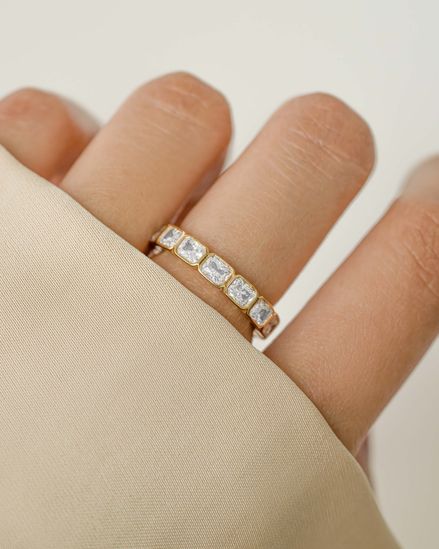 Sami Jewels bezel emerald cut eternity band ring with gold setting, showcasing a continuous row of emerald-cut gemstones.