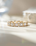 Gold Sami Jewels bezel emerald cut eternity band ring with detailed gemstone accents.
