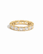 Gold bezel emerald cut eternity band ring from Sami Jewels on a white background.