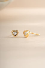 Gold bezel heart stud earrings from Sami Jewels, shown in an angled view highlighting their delicate design and polished finish.