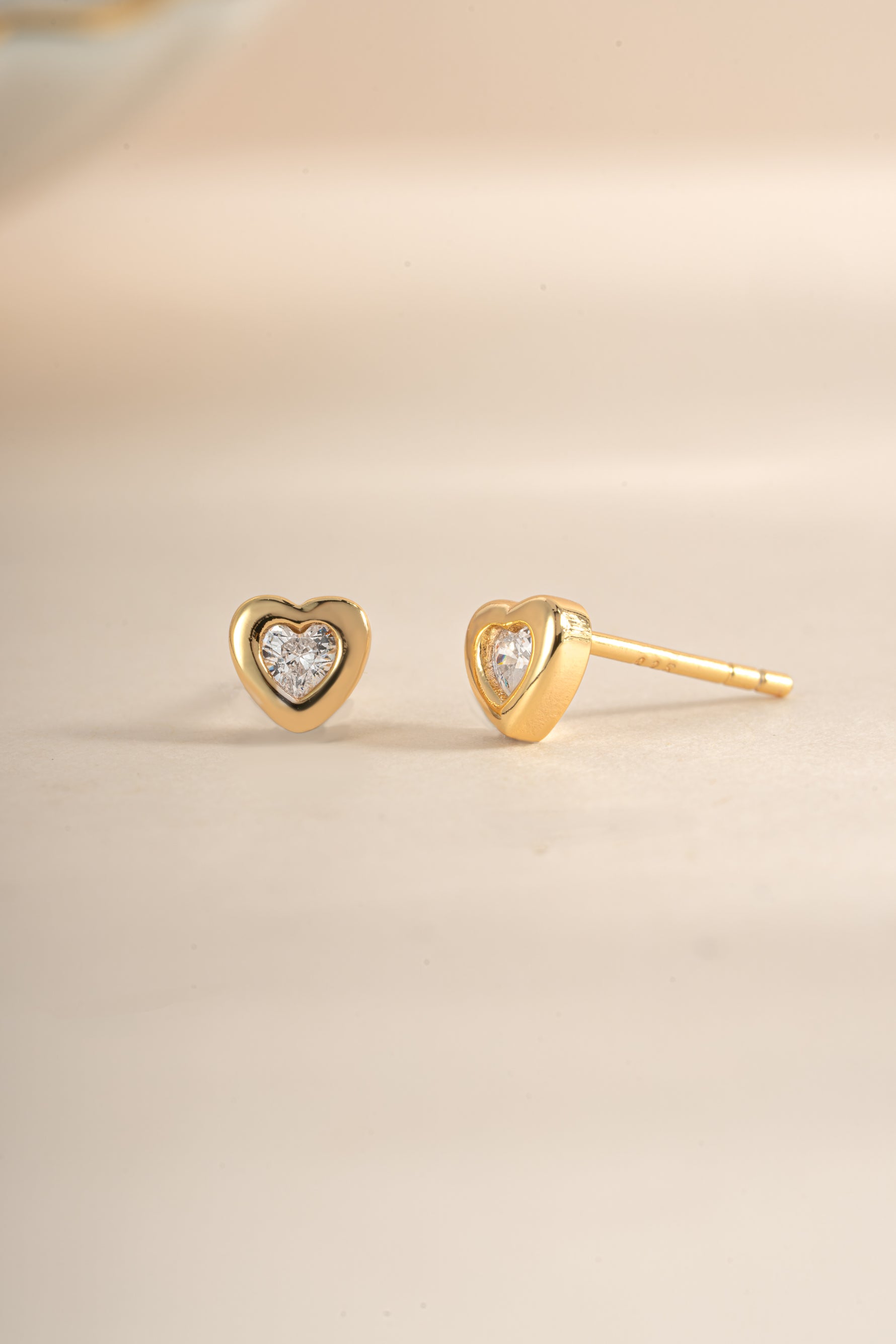 Gold bezel heart stud earrings from Sami Jewels, shown in an angled view highlighting their delicate design and polished finish.