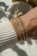 Gold Sami Jewels bezeled baguette tennis bracelet stacked on a model's wrist, showcasing elegant jewelry design.