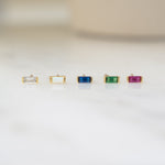 closeup of tiny birthstone earrings including a white cubic zirconia stud earring, an opal stud earring, a sapphire stud earring, an emerald stud earring and a ruby stud earring
