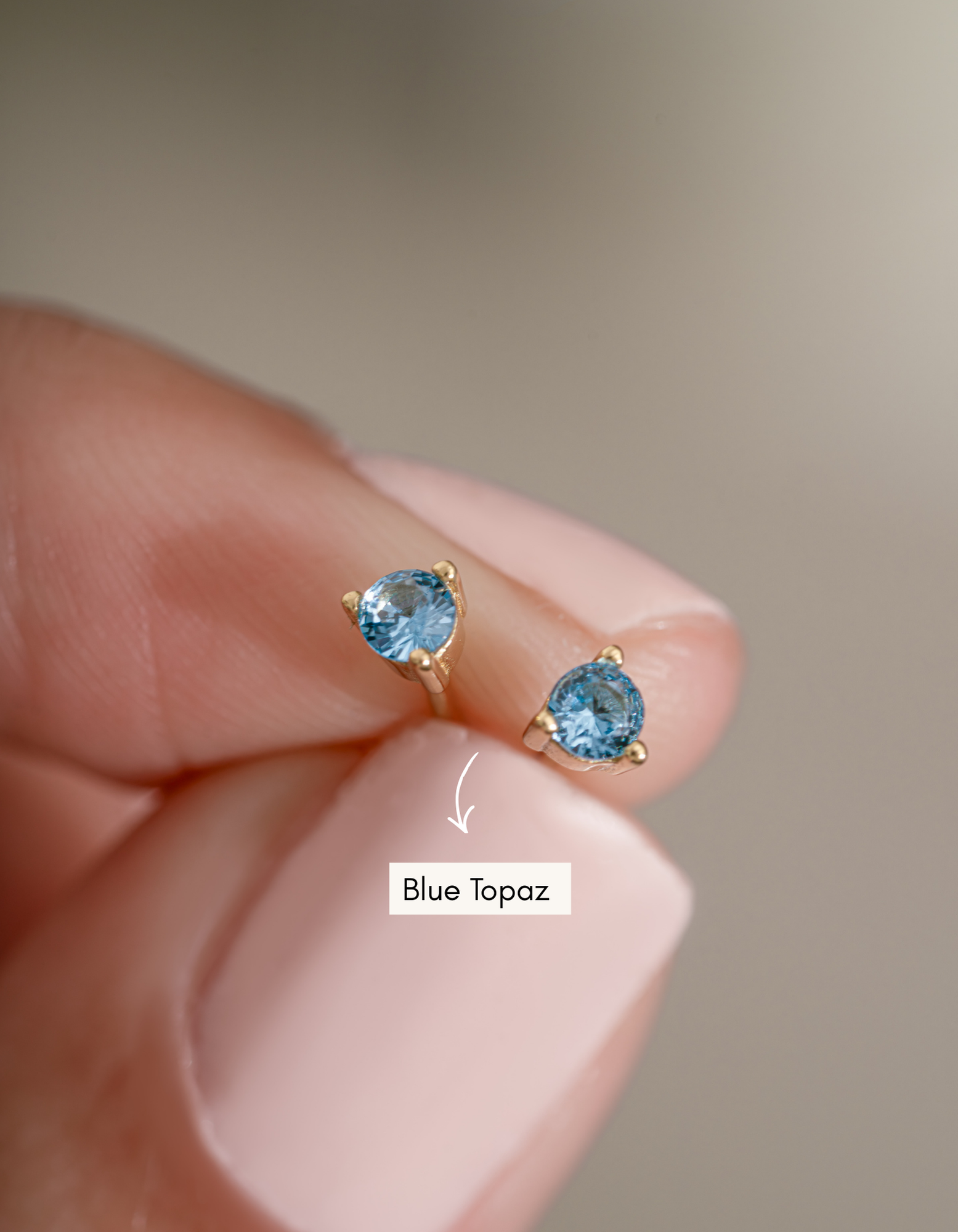 gold blue topaz stud earrings in between fingers