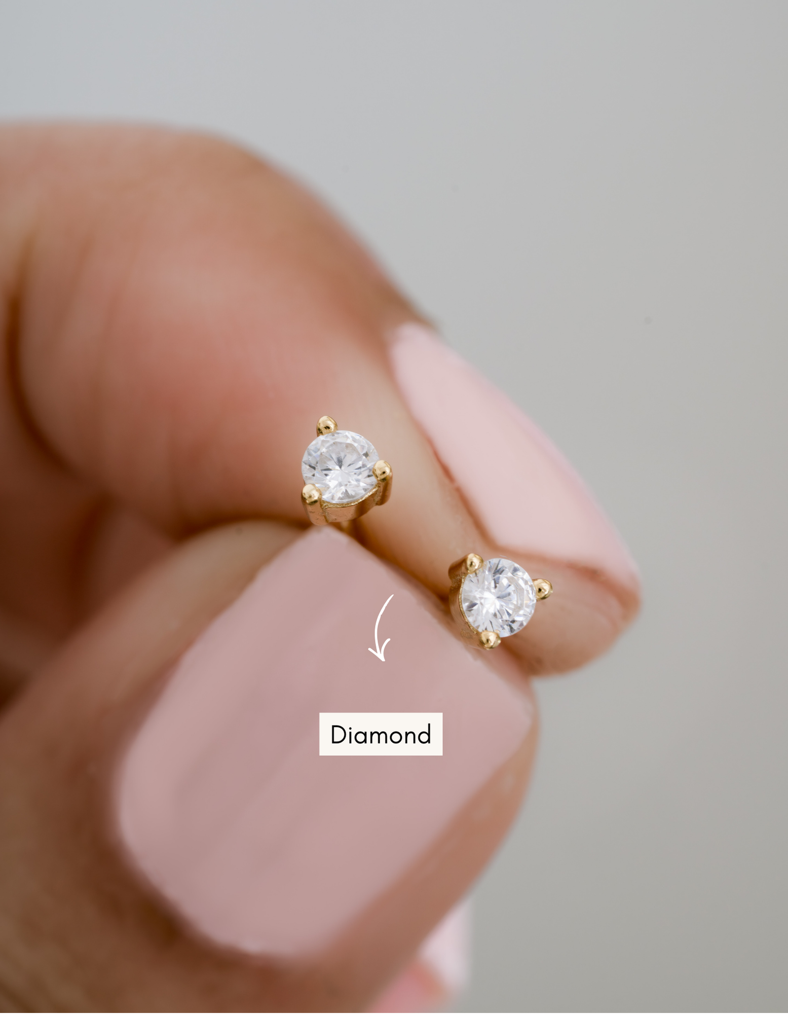 gold diamond stud earrings in between fingers