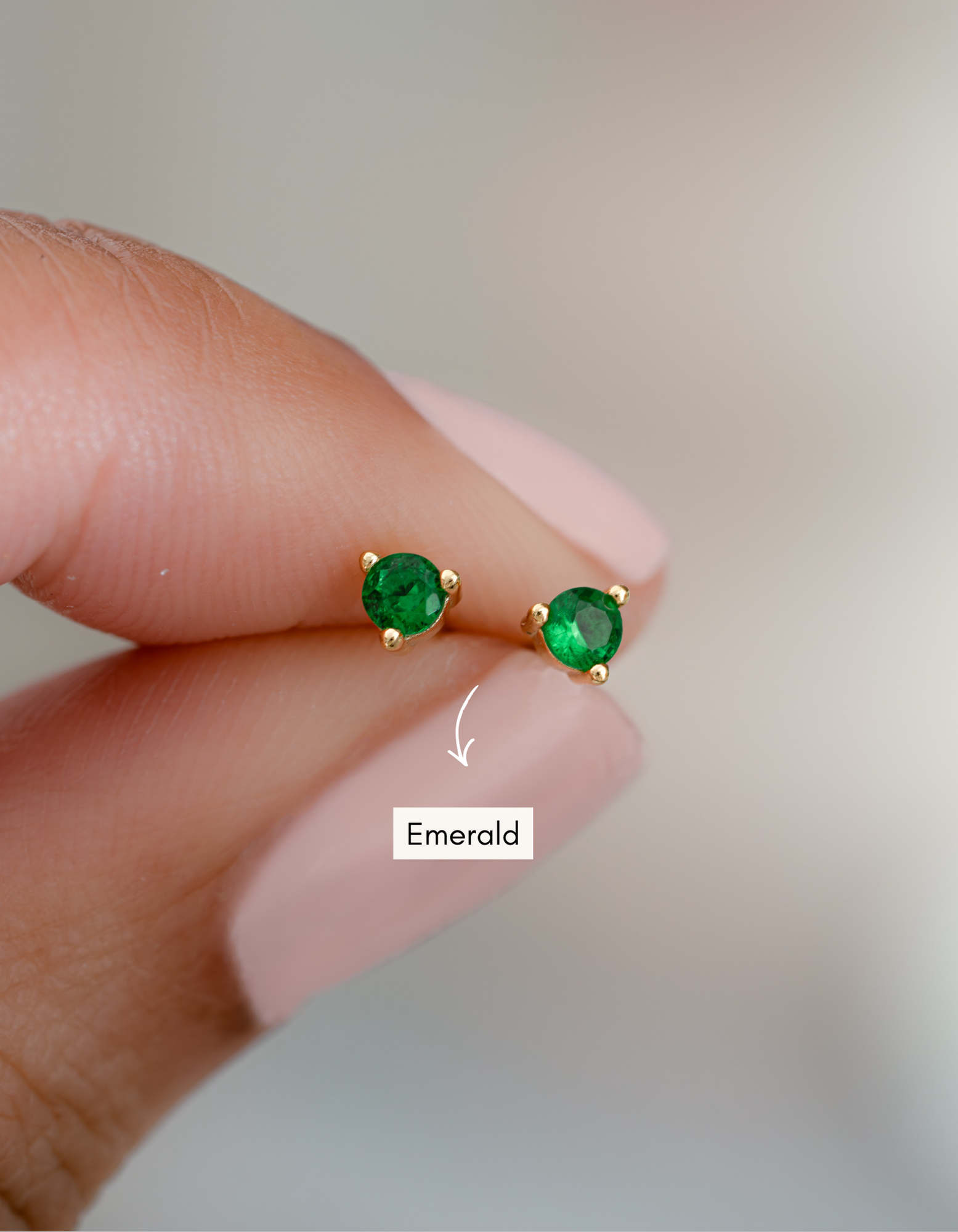 gold emerald green stud earrings in between fingers