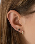 Black flower stud earrings by Sami Jewels featuring gold-tone accents, shown on a model's ear.