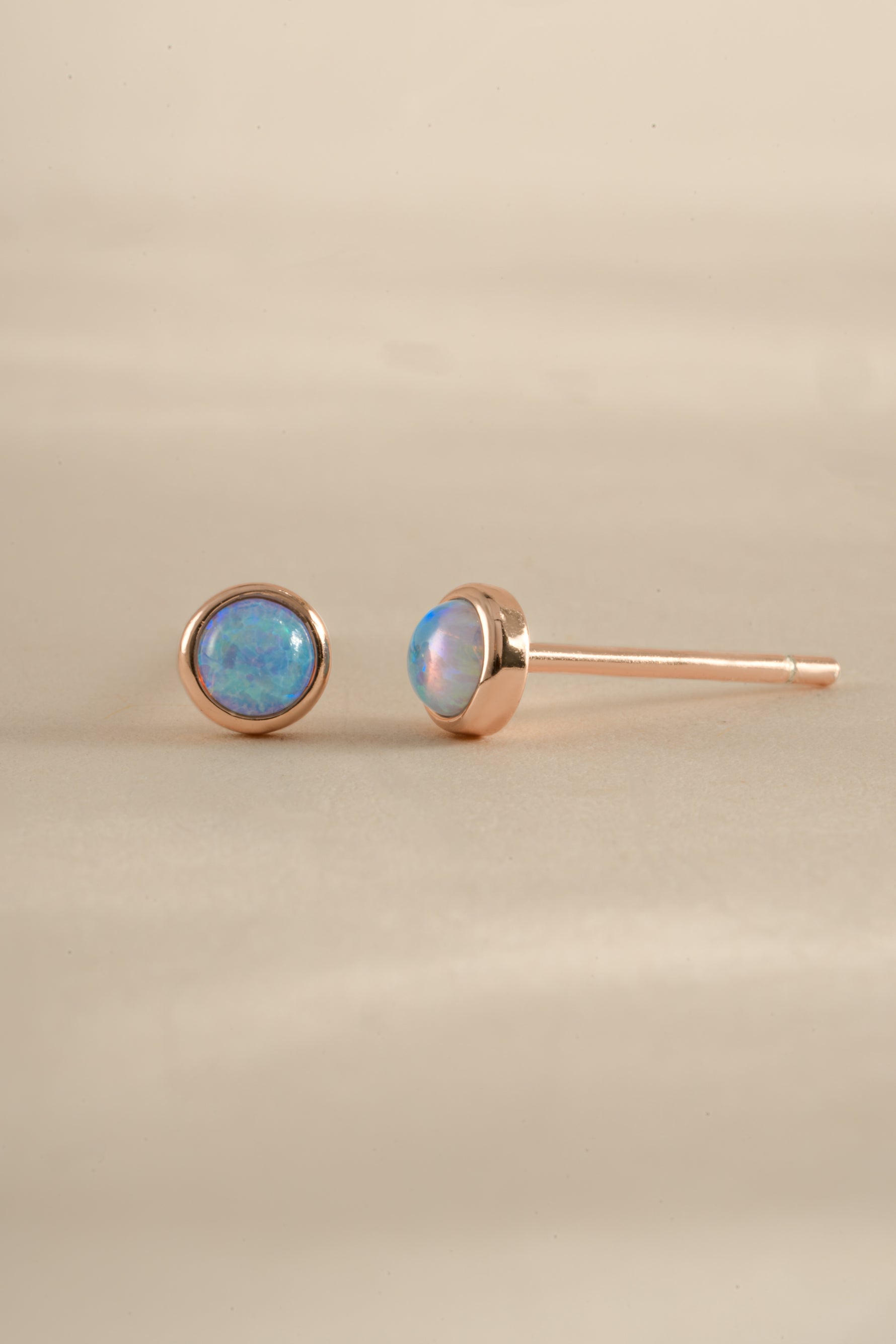 Blue Opal Stud Earrings by Sami Jewels featuring rose gold settings and round blue opal gemstones.