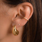 model wearing dangling teardrop earrings with a silky, polished surface layered with gold stud earrings and diamond huggie hoop earrings