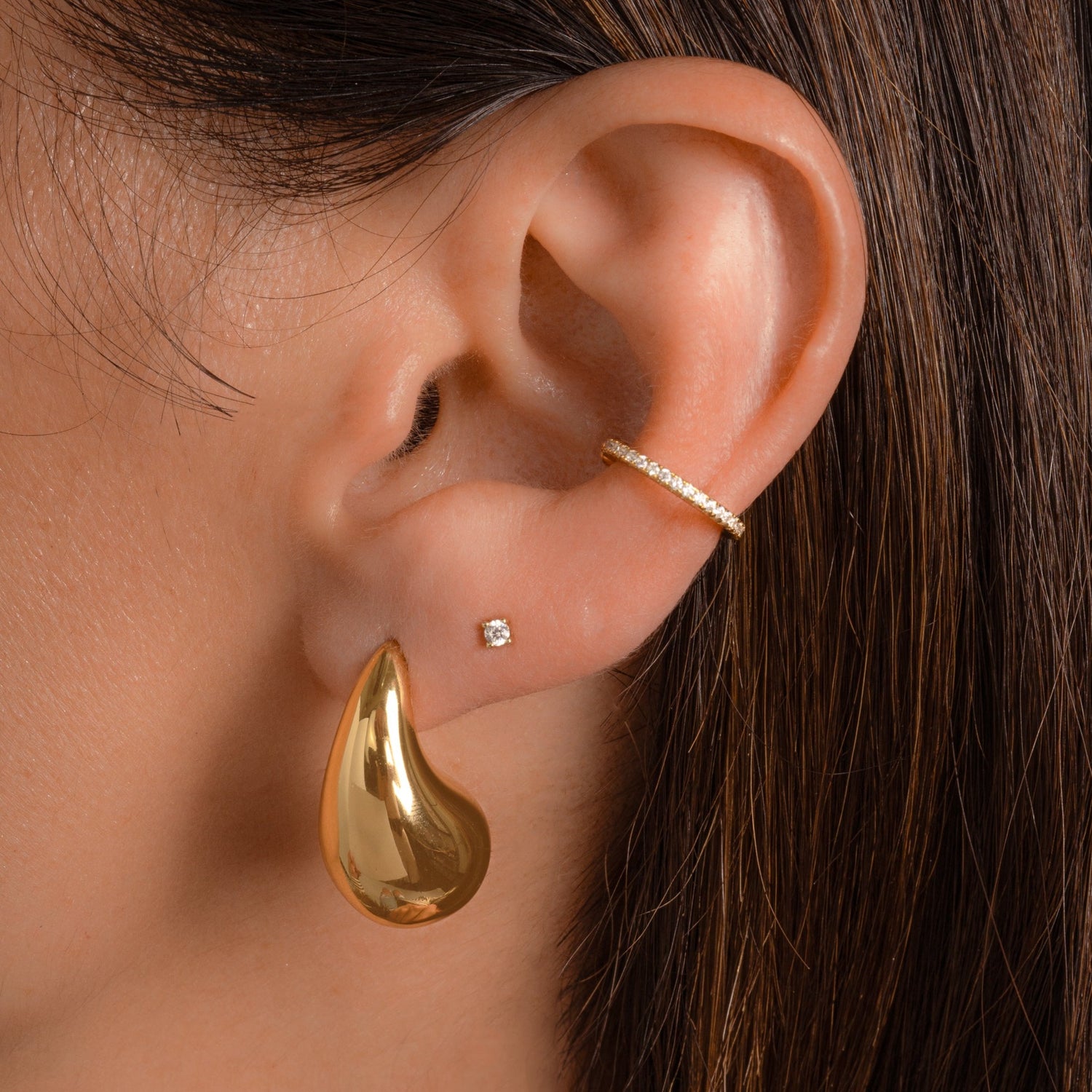 model wearing dangling teardrop earrings with a silky, polished surface layered with gold stud earrings and diamond huggie hoop earrings