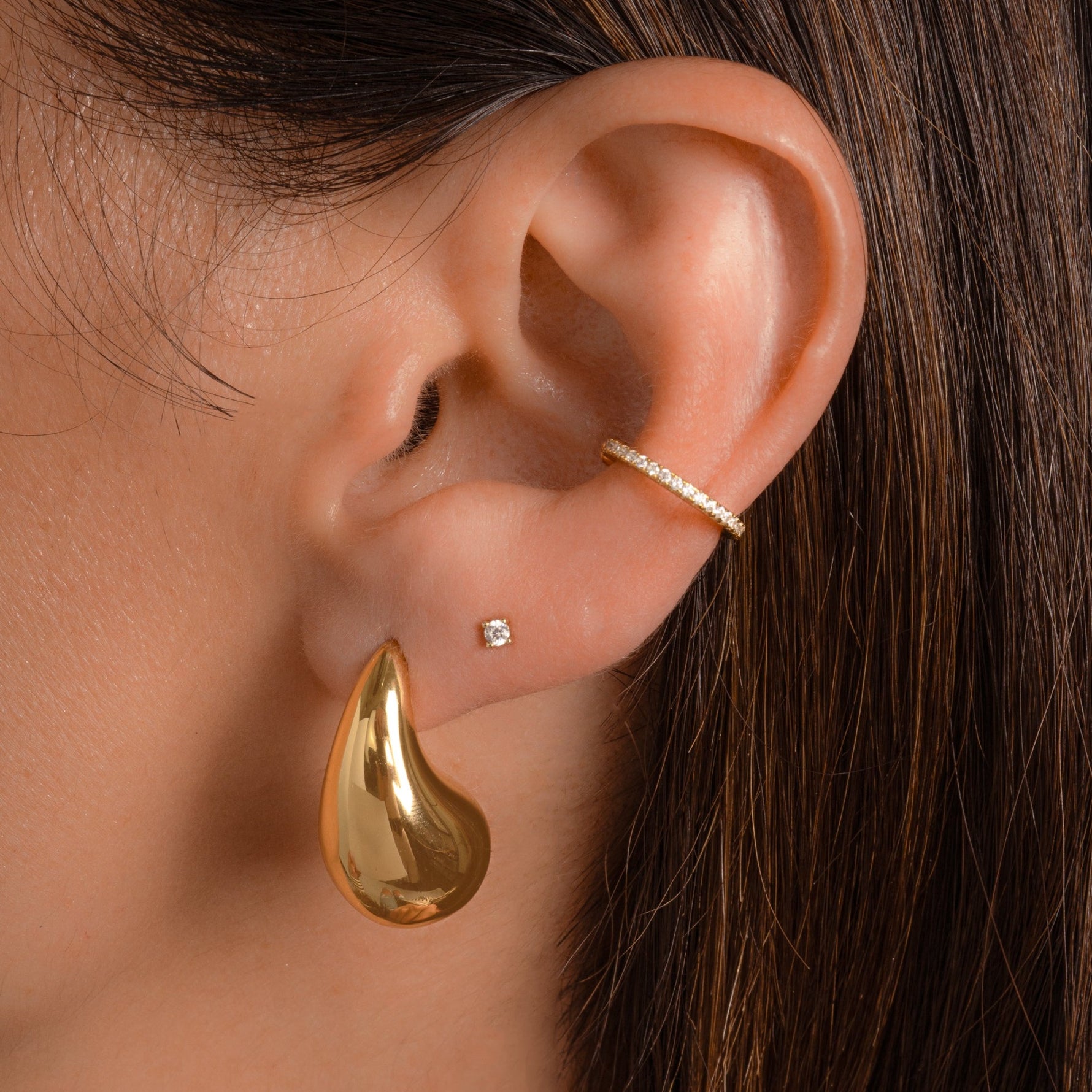 model wearing dangling teardrop earrings with a silky, polished surface layered with gold stud earrings and diamond huggie hoop earrings