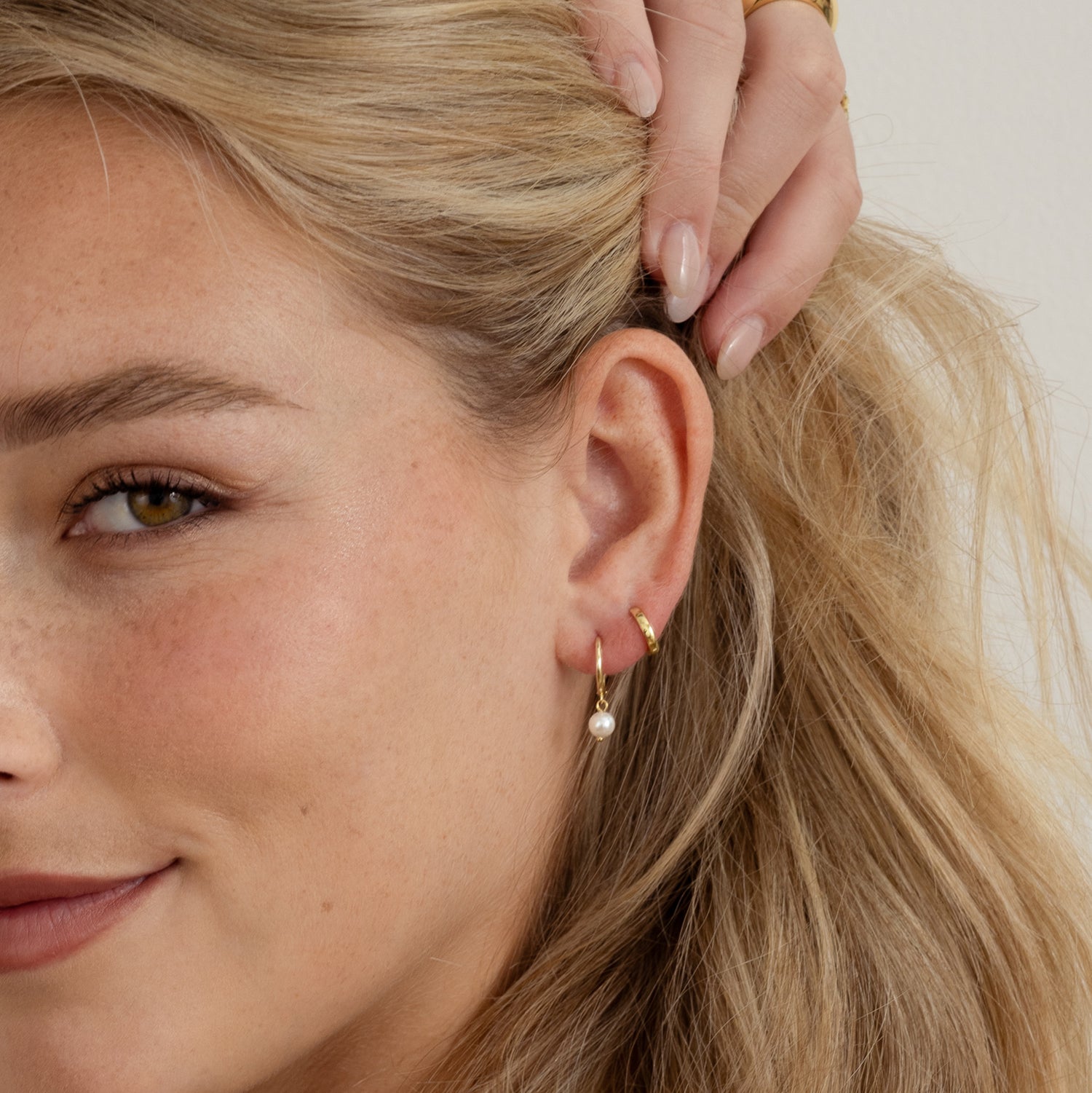 Model wearing dainty gold pearl charm huggies and tiny gold hoop earrings