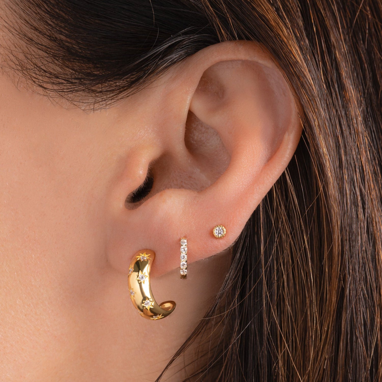 model wearing gold hoop earrings, diamond huggies, and a tiny diamond stud on her third piercing. The  hoop earrings are small hoops are celestial hoop earring design.