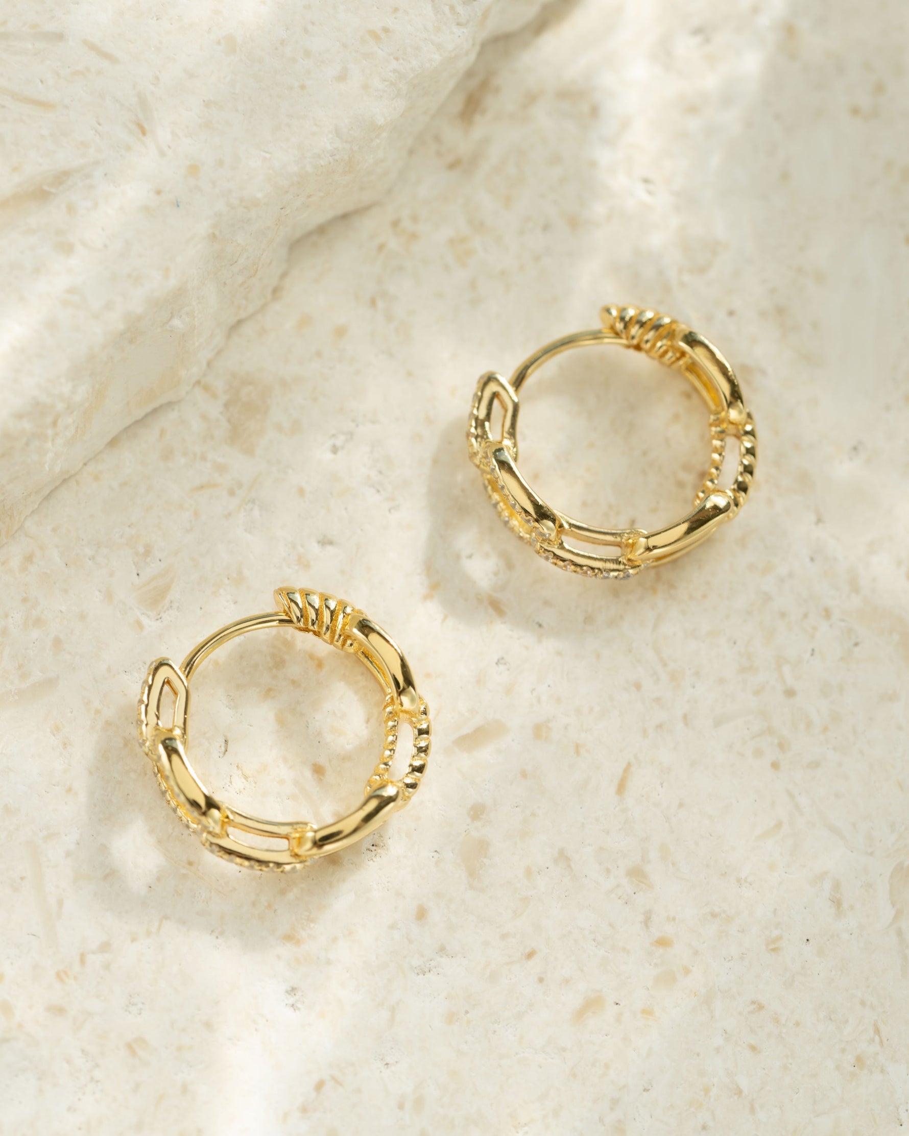 Small chain link hoop earrings by Sami Jewels, showing a close-up profile view of the silver metal hoops with intertwined links.