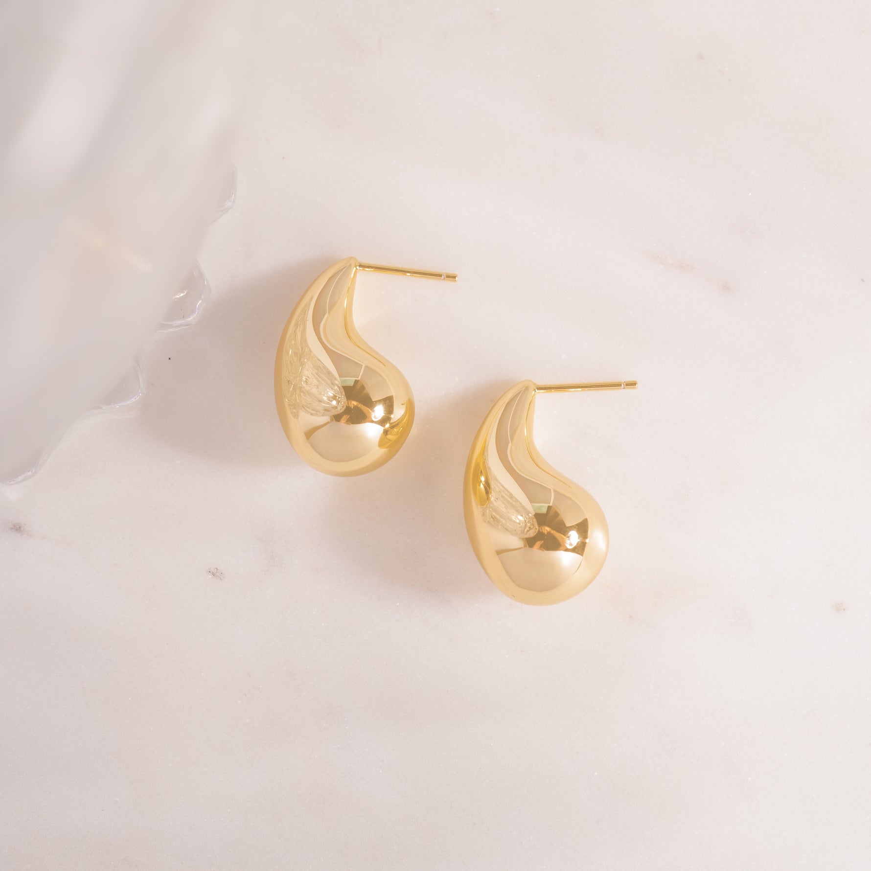 flay lay of a teardrop earrings with a bold sculptural feel, soft, rounded curves of high-shine silver that taper into a silky, weightless drop.