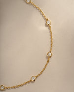 Close-up of the gold anklet's round bezel-set stones and fine cable chain.