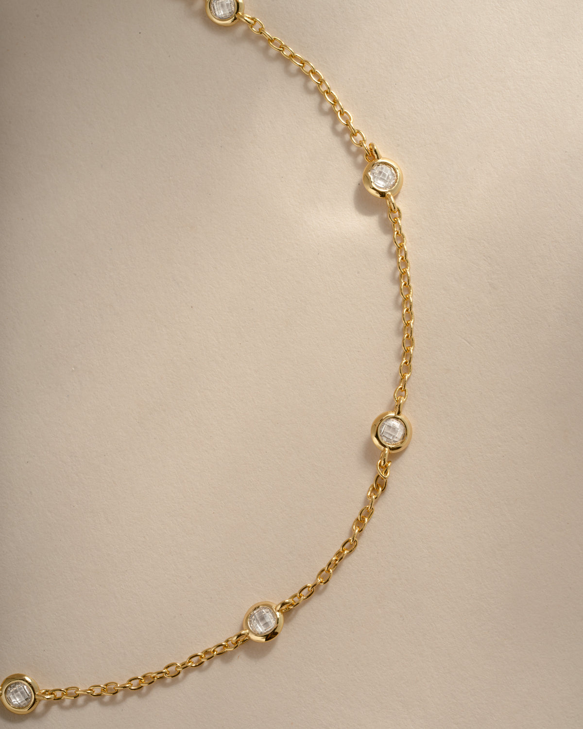 Close-up of the gold anklet's round bezel-set stones and fine cable chain.