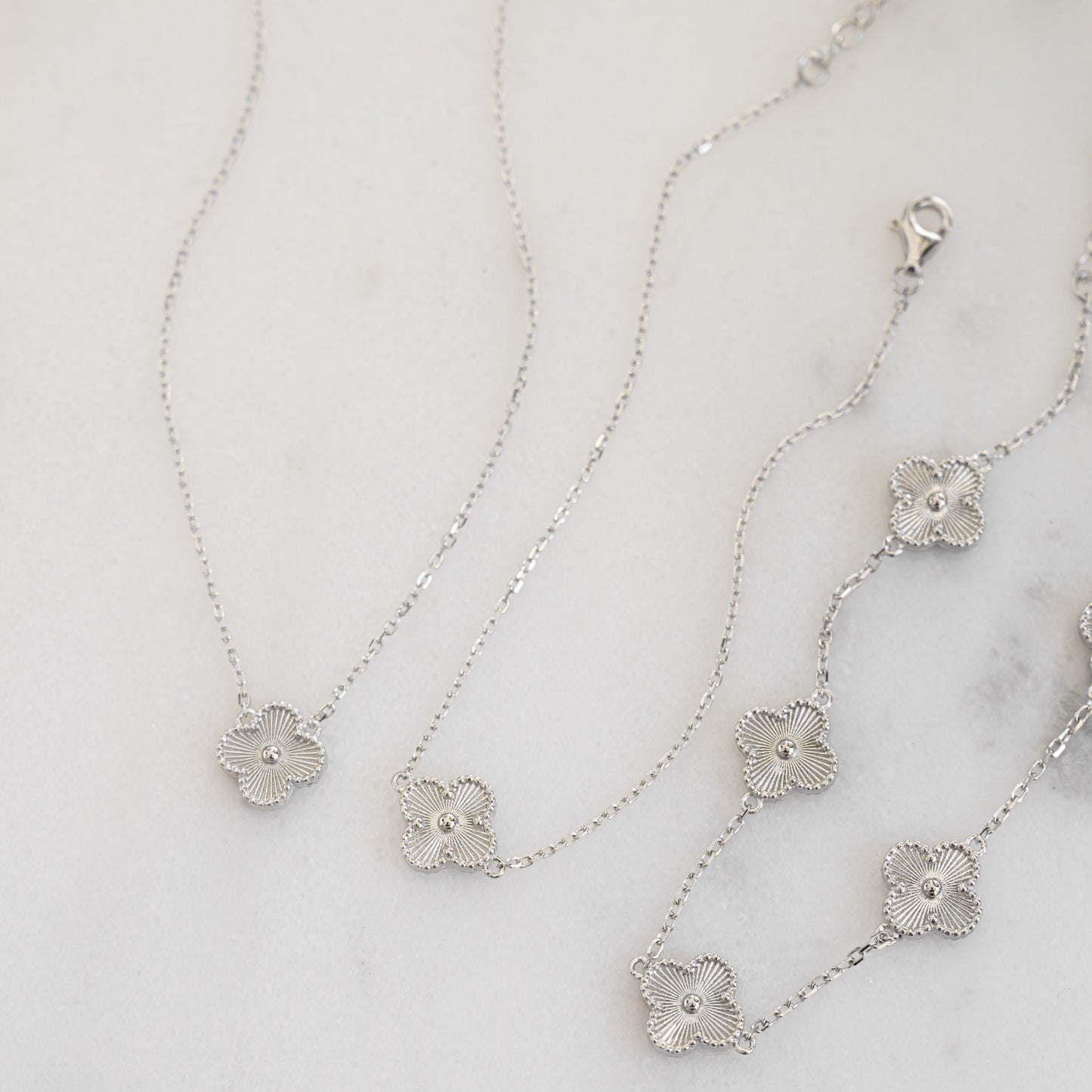 flat lay of four leaf clover necklace in silver along with silver matching bracelets.