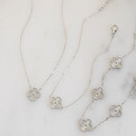 flat lay of four leaf clover necklace in silver along with silver matching bracelets.