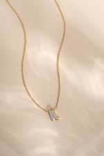A delicate gold chain necklace featuring a small boot-shaped pendant encrusted with clear stones, displayed on a soft, light beige fabric background.