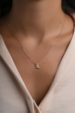 A delicate gold chain necklace with a small cowboy boot pendant featuring clear stones, worn by a model in a cream-colored blouse.