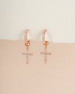 Rose gold CZ cross charm huggie earrings by Sami Jewels featuring small hoop design with dangling cross charms.