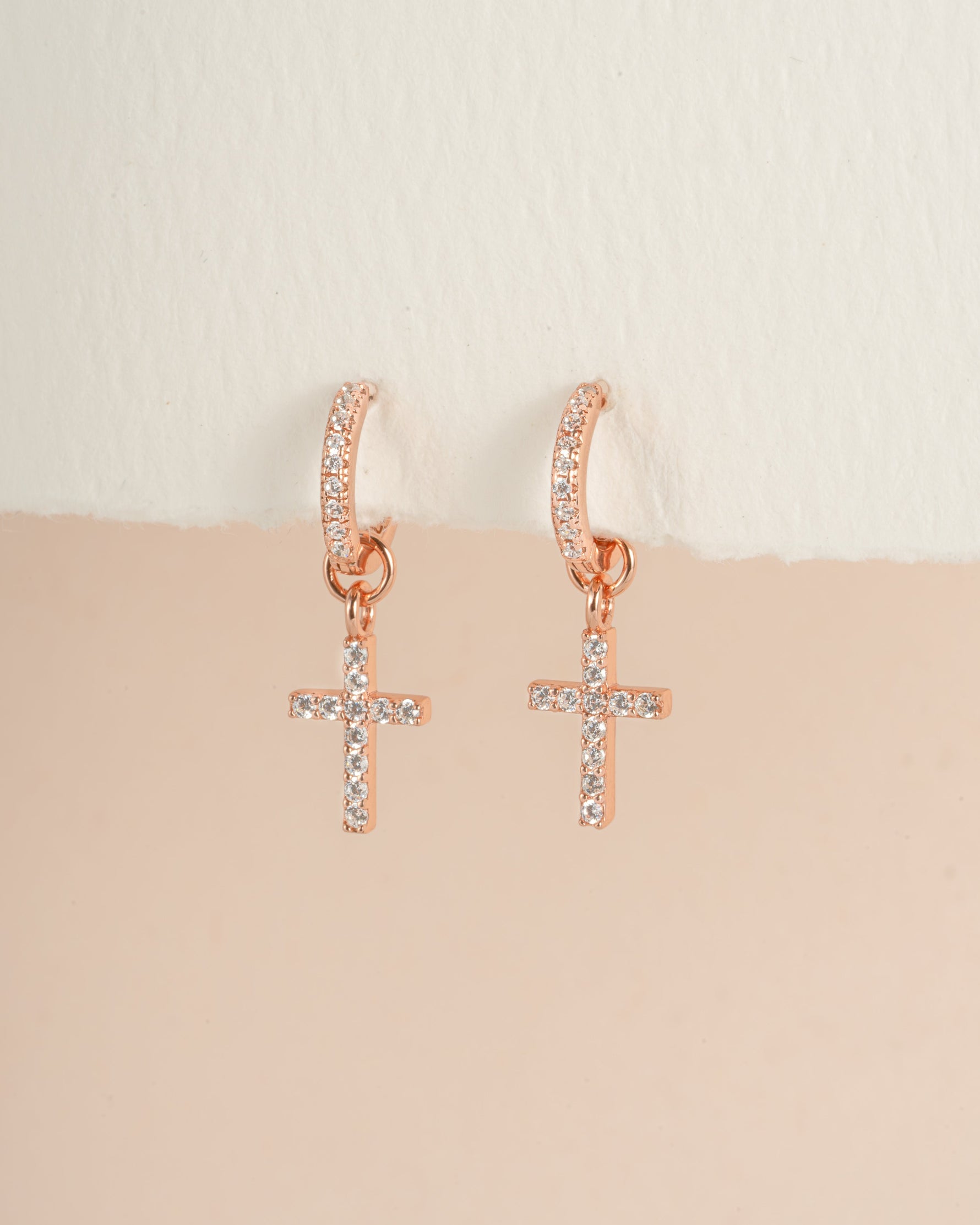 Rose gold CZ cross charm huggie earrings by Sami Jewels featuring small hoop design with dangling cross charms.
