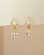 Gold cross and dagger charm huggie earrings by Sami Jewels featuring small hoop design with intricate charms.