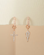 Rose gold cross and dagger charm huggie earrings by Sami Jewels, showing front view with detailed charms on small hoop earrings.