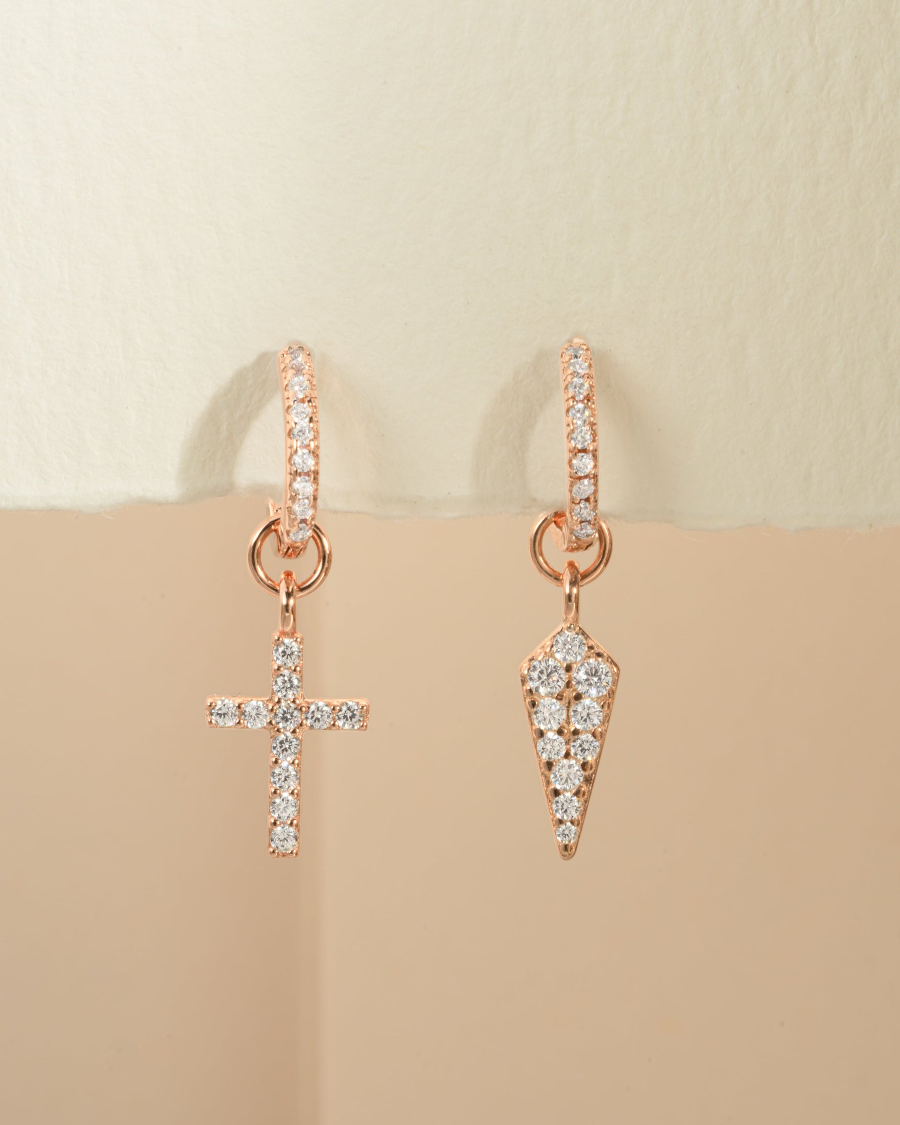 Rose gold cross and dagger charm huggie earrings by Sami Jewels, showing front view with detailed charms on small hoop earrings.