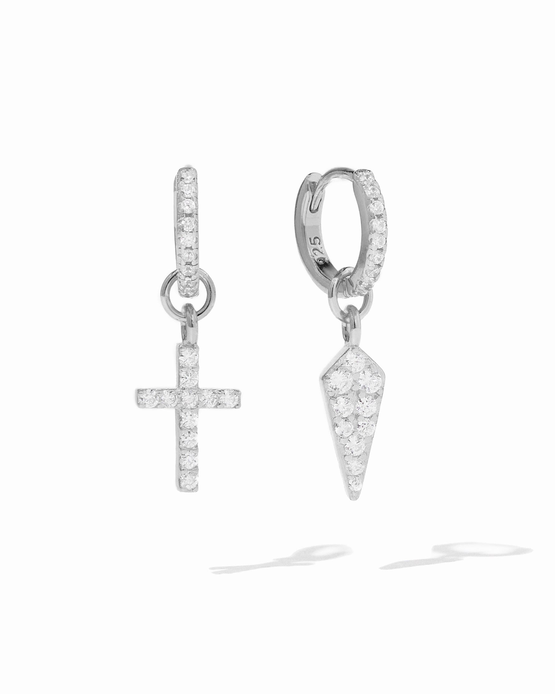 Sterling silver cross and dagger charm huggie earrings by Sami Jewels on a white background.