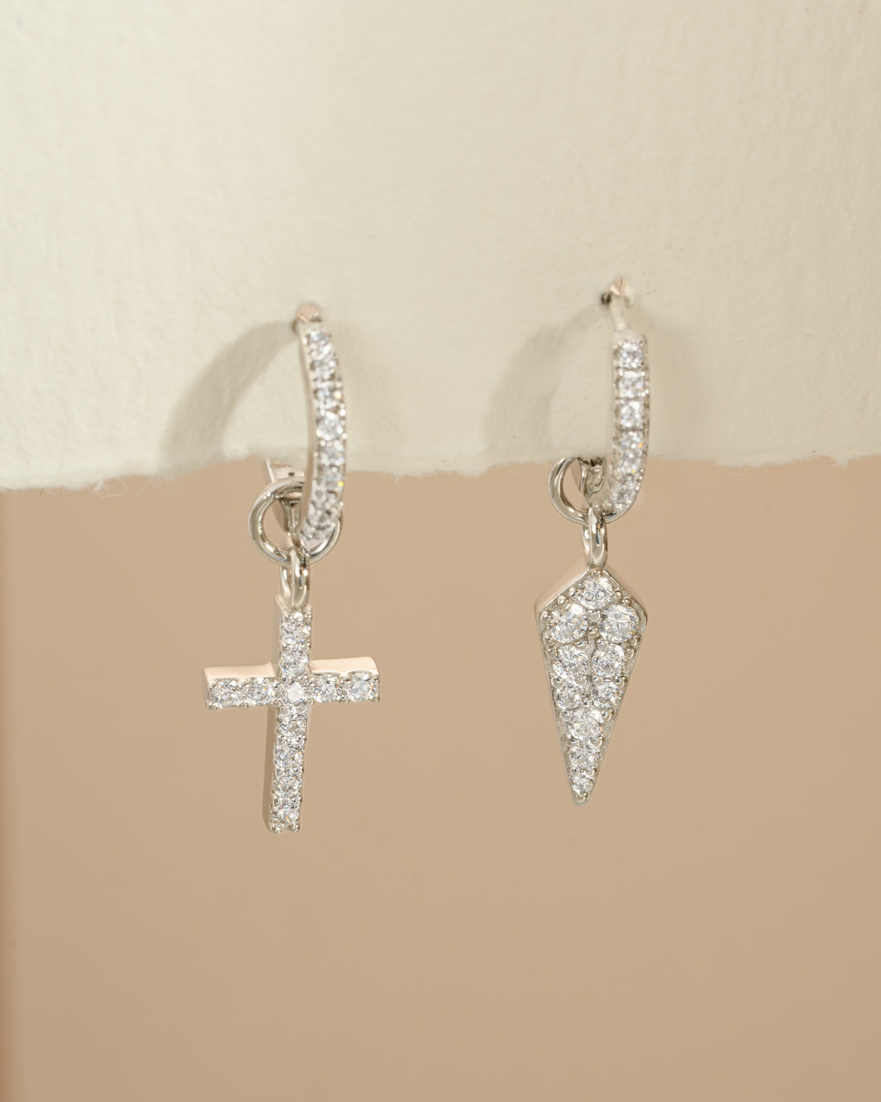 Sterling silver Sami Jewels cross and dagger charm huggie earrings with detailed design and secure hoop closure.