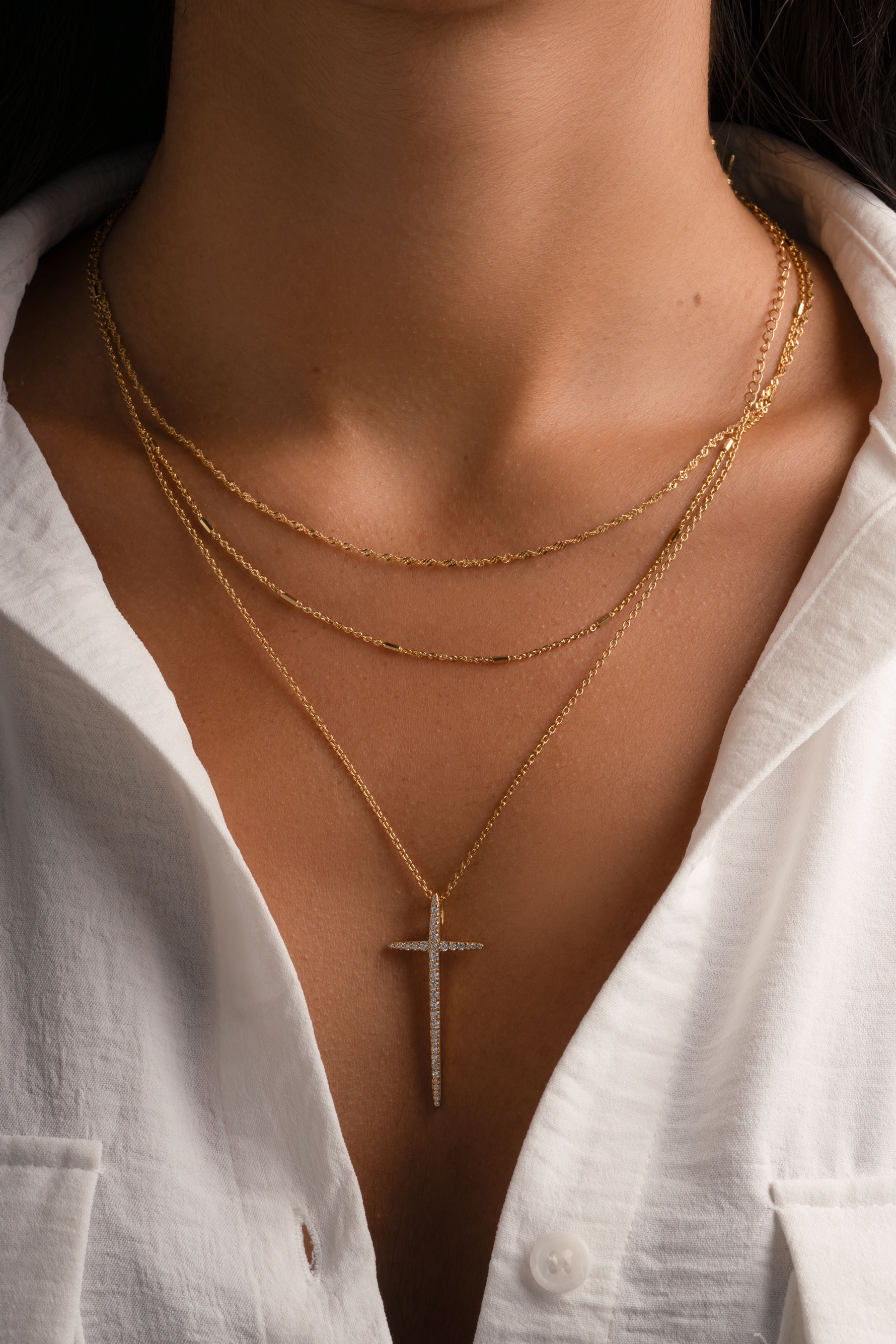 Gold cross necklace by Sami Jewels featuring a sleek pendant worn on a chain, styled on a model.