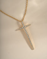 Close-up of a gold Sami Jewels cross necklace showcasing detailed design and elegant chain on a neutral background.
