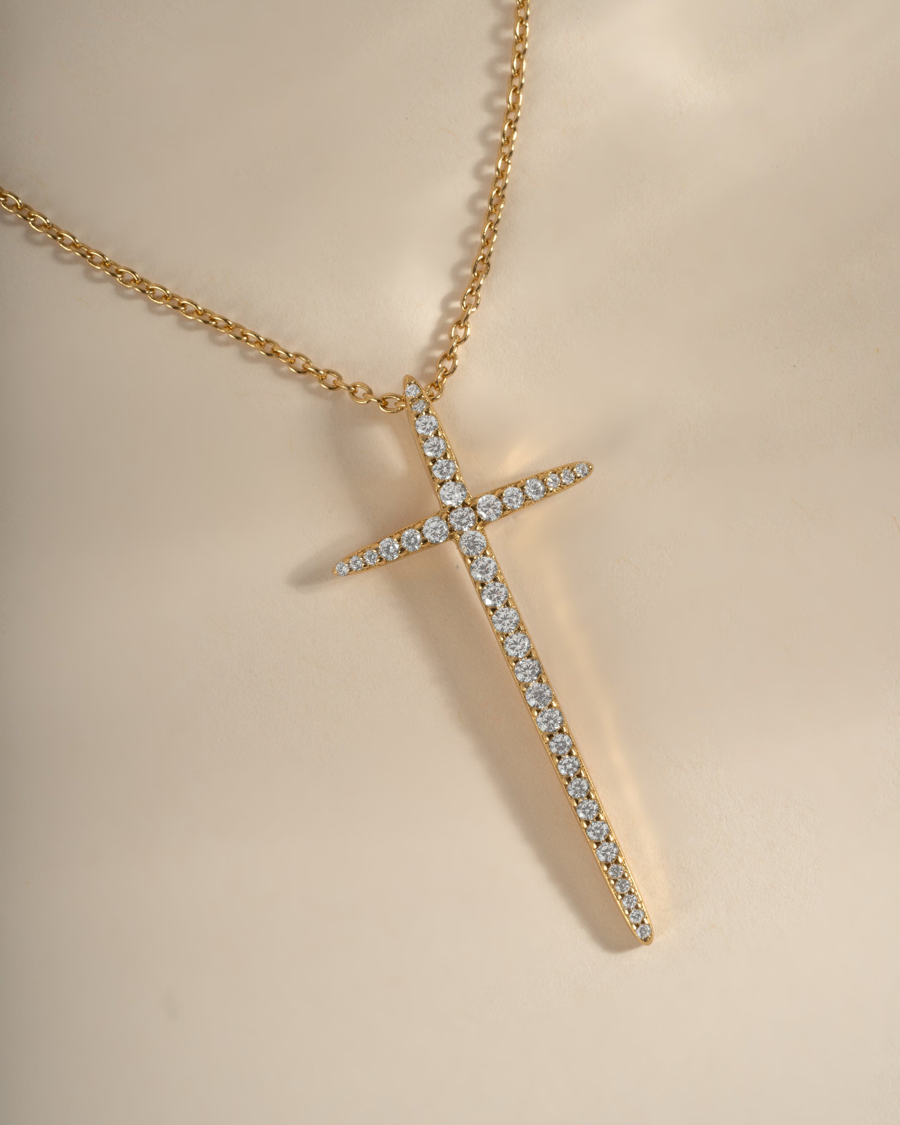 Close-up of a gold Sami Jewels cross necklace showcasing detailed design and elegant chain on a neutral background.
