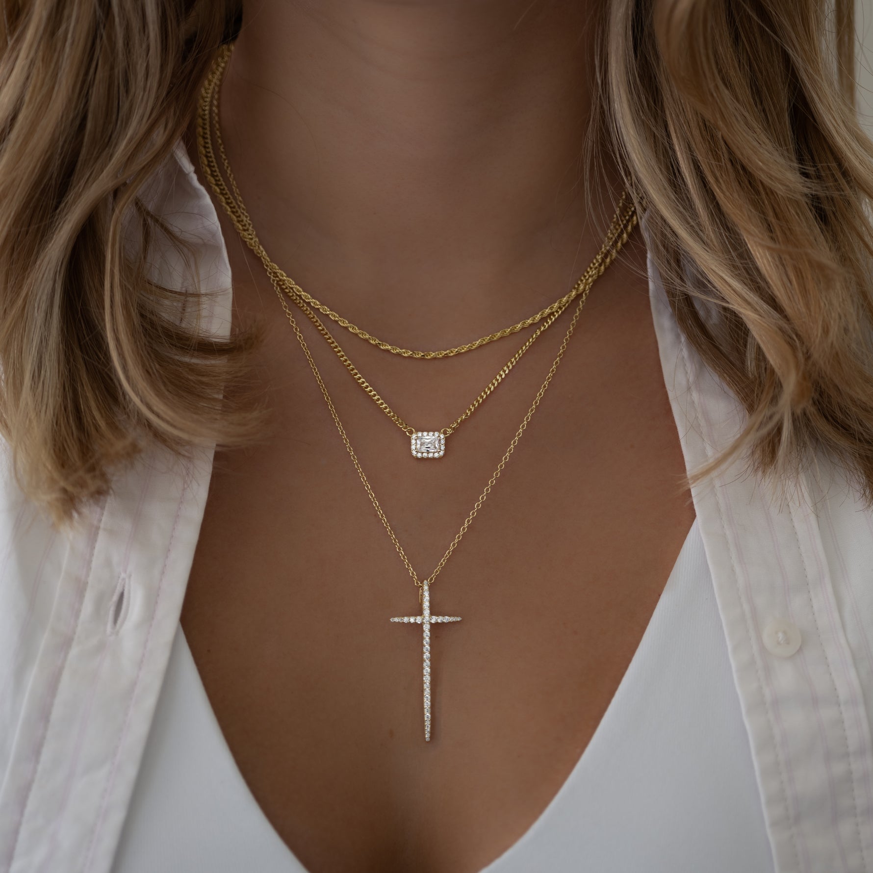 Cubic zirconia halo emerald cut necklace styled on model, with minimalist gold chain necklace and a statement diamond cross pendant necklace, perfect for layering or solo wear