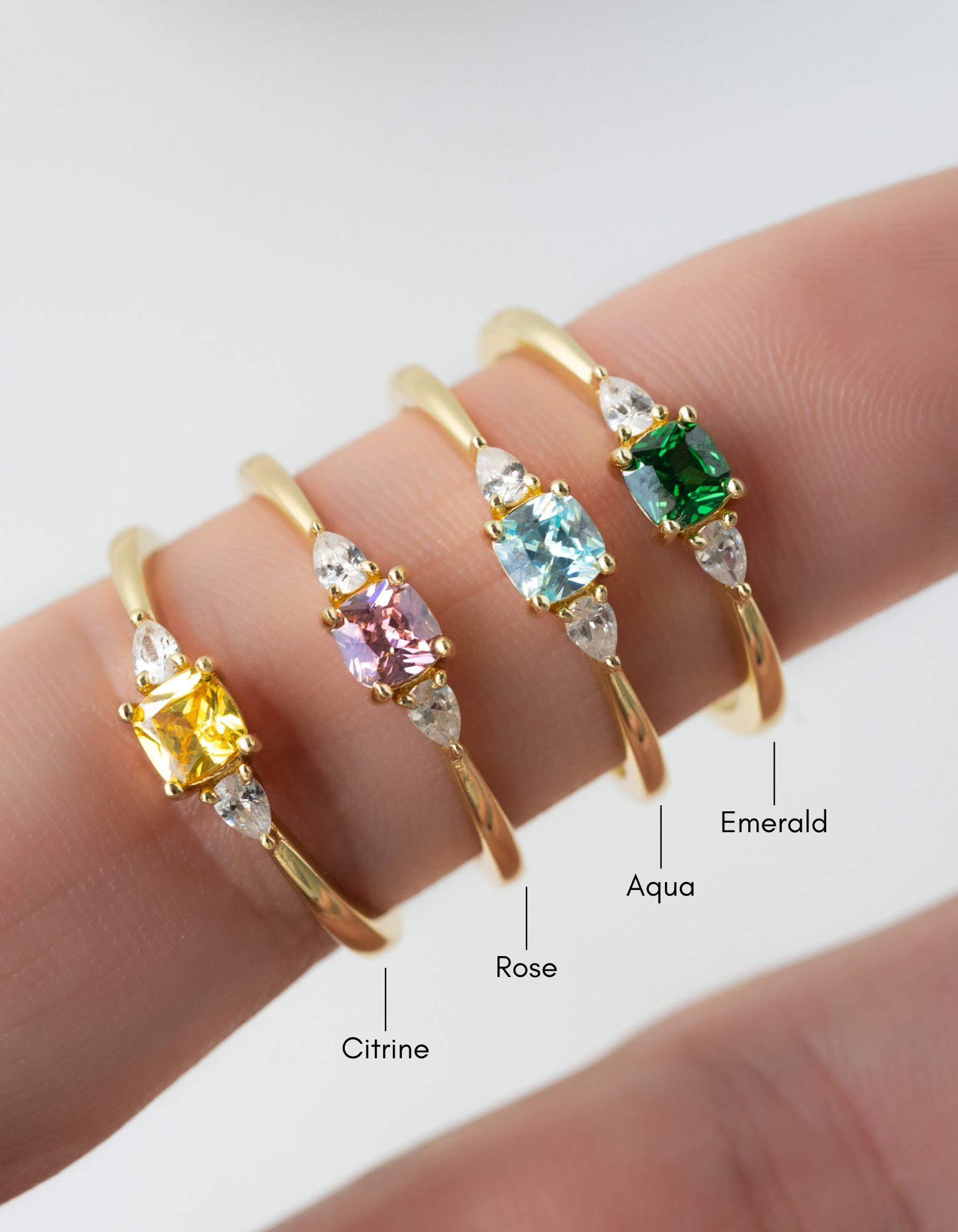 cushion diamond ring in yellow, pink, aqua, and emerald on a finger