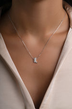 A close-up of a model wearing a delicate silver chain necklace with a small cowgirl, western themed pendant set with clear stones, paired with a cream-colored satin blouse.