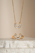 Gold horseshoe jewelry set including a necklace and ring with cubic zirconia details from Sami Jewels.