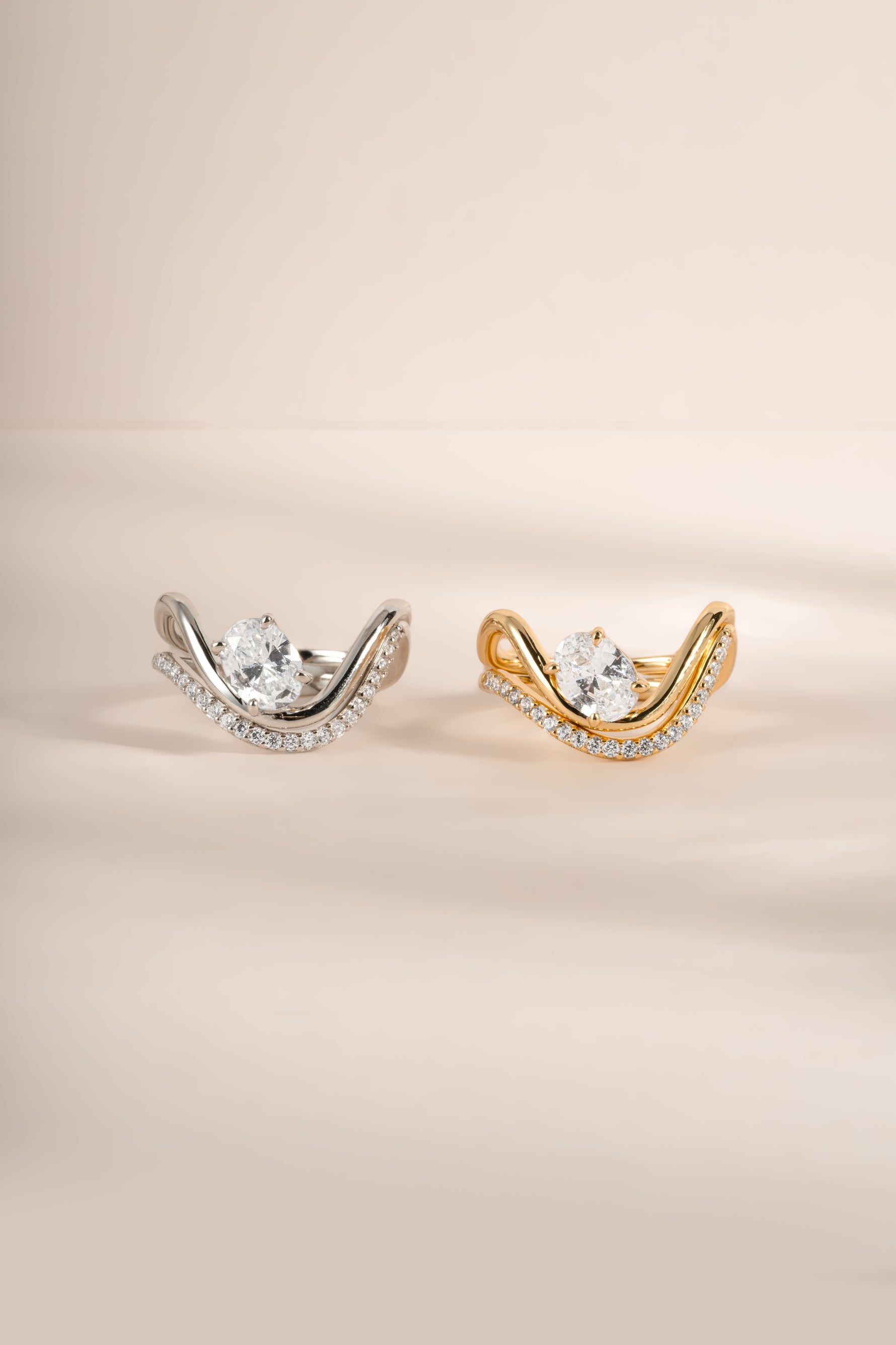 Close-up side by side image of gold and silver wavy oval diamond ring sets with pavé bands. 