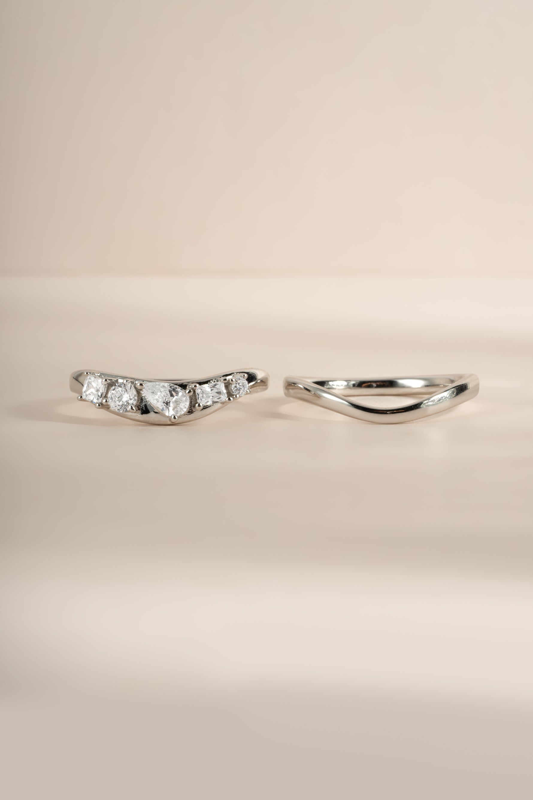 Up-close image of silver wavy ring set, showing both rings in the set, side by side. Left ring features 5 cz stones and right ring is plain gold. 