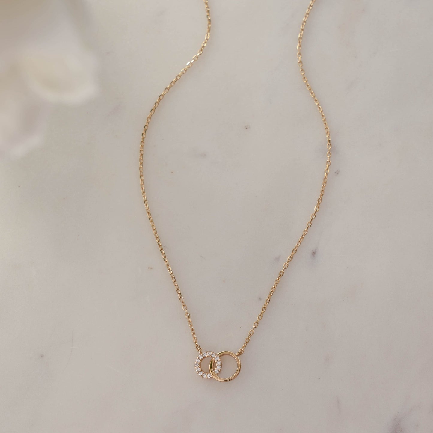 Delicate 14k gold plated love link necklace on white marble background.