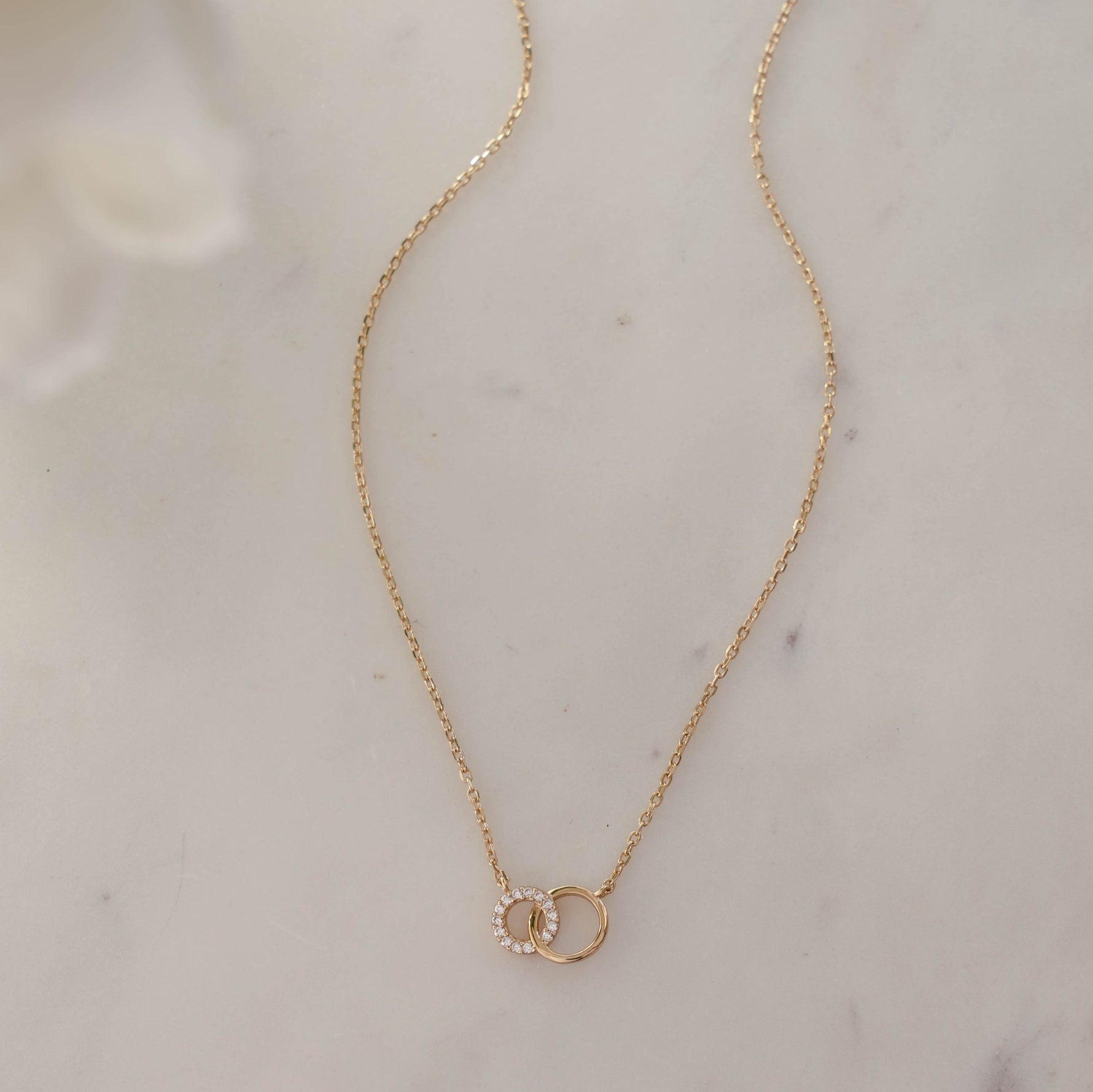 Delicate 14k gold plated love link necklace on white marble background.