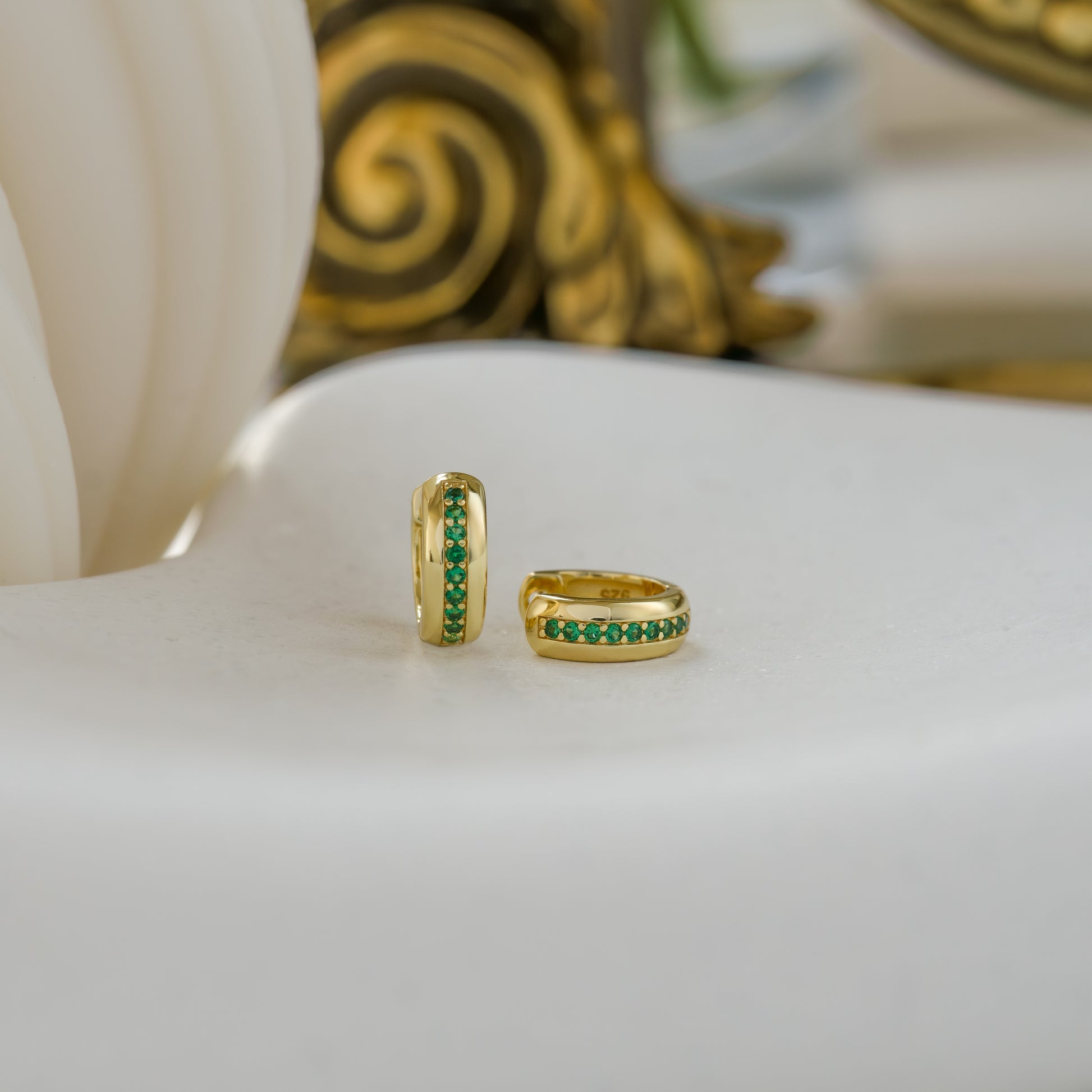 a close up of a pair of small gold hoop earrings featuring emerald gemstones