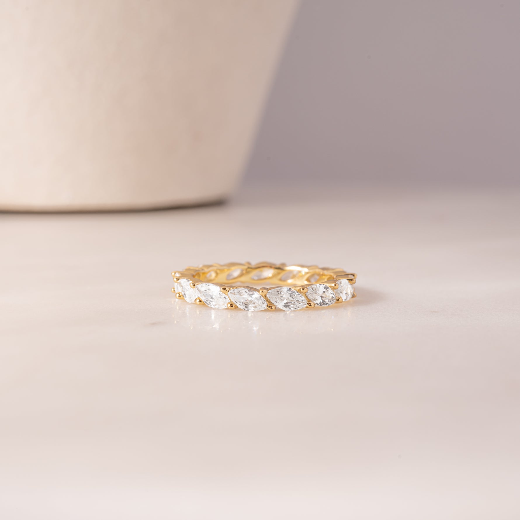 flat lay of a 14k gold ring highlighting its continuous row of sparkling gemstones set in gold, offering a mix of smooth and textured finishes.